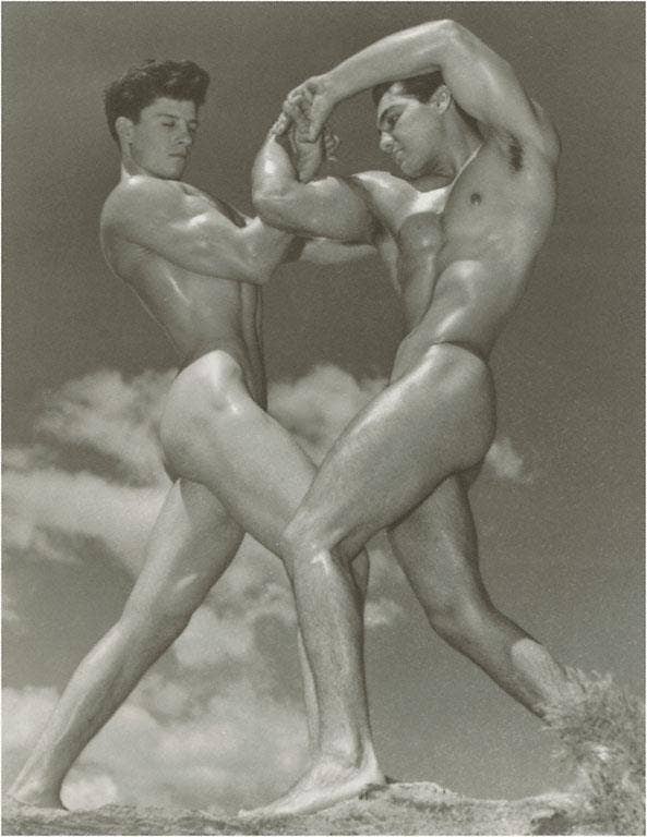 Black and white photograph of two nude men in a dynamic pose against a cloudy sky.