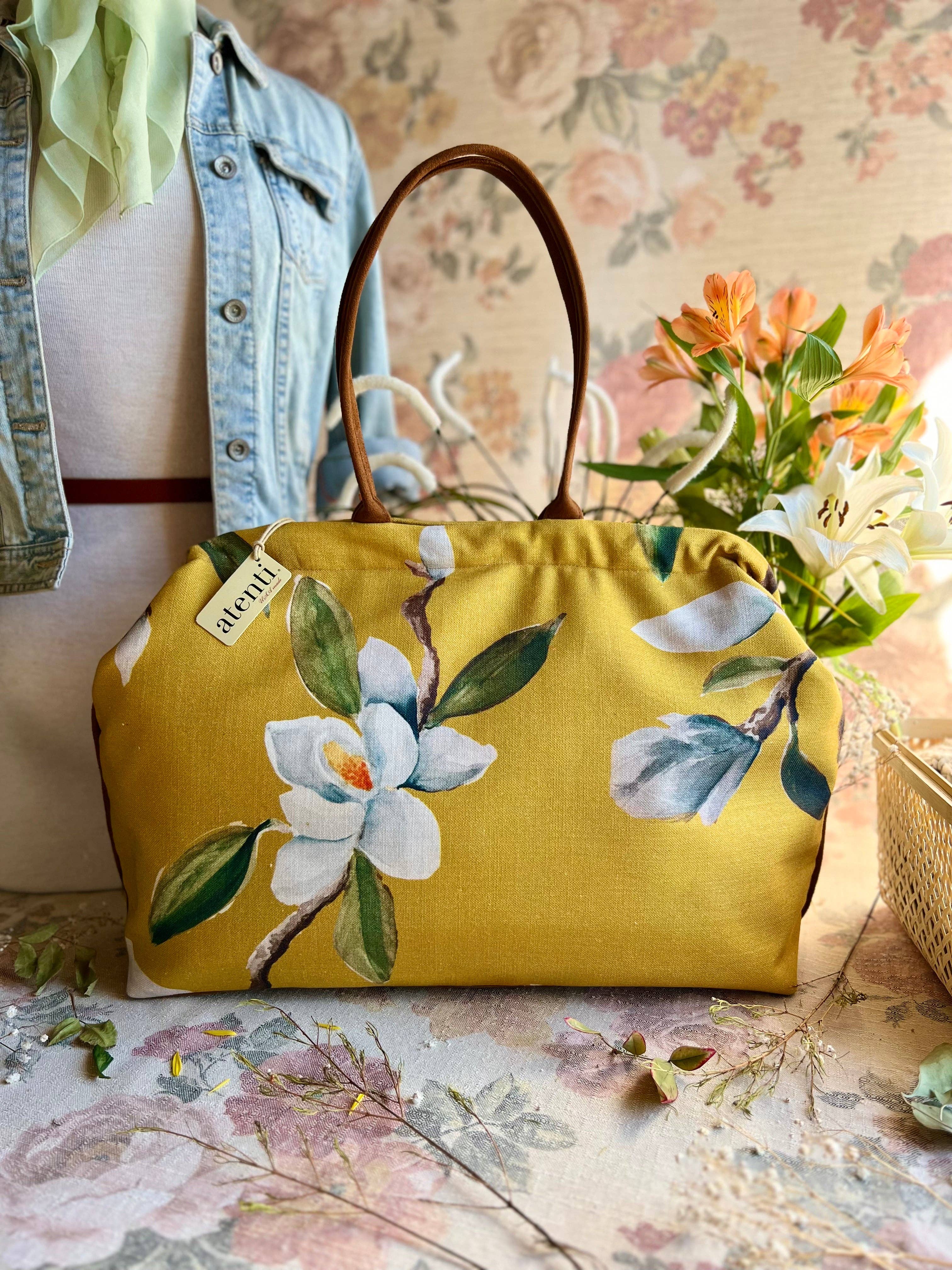 Yellow floral handbag on a floral-patterned surface with a denim jacket and flowers in the background.