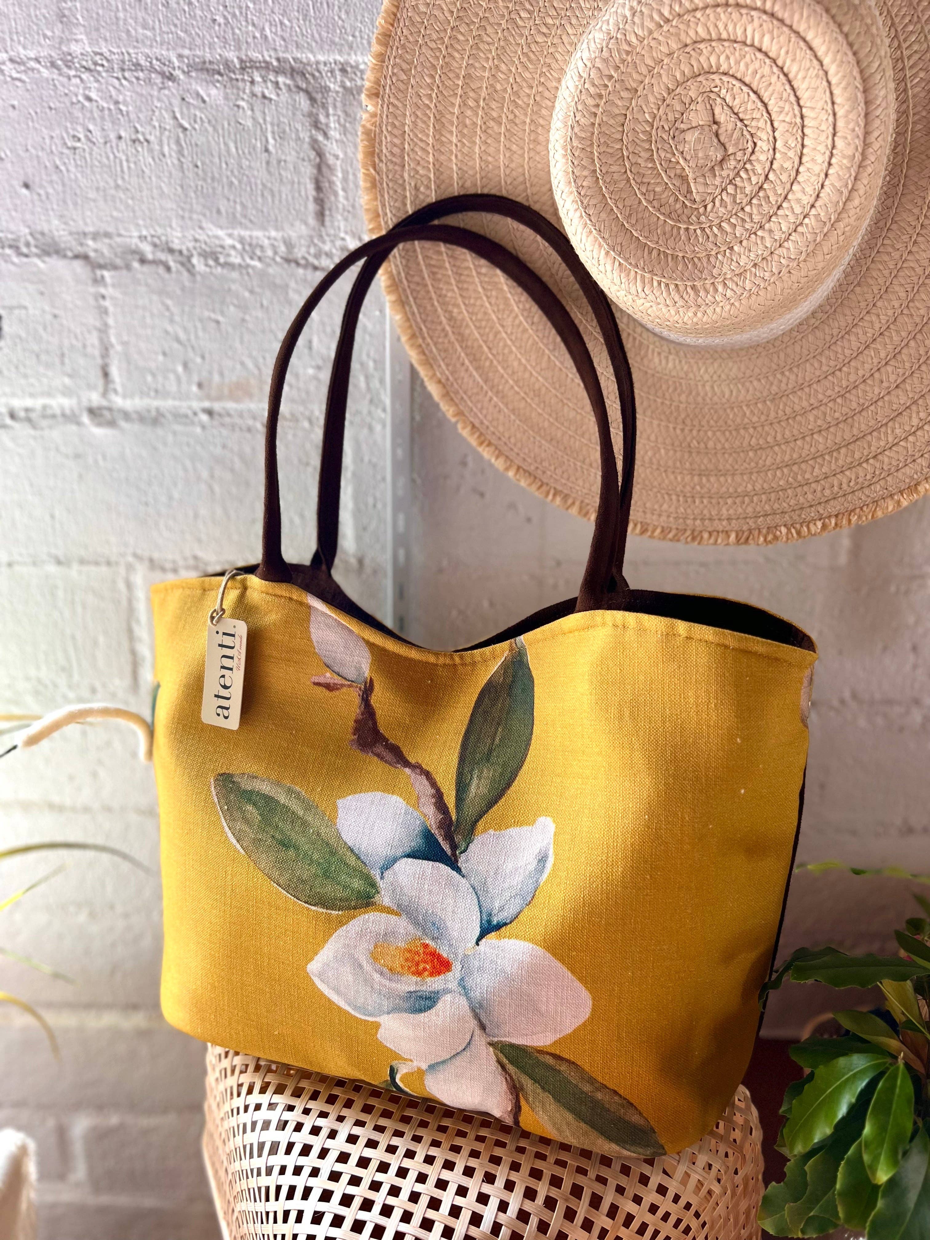 Yellow tote bag with floral design and straw hat on a white brick wall background