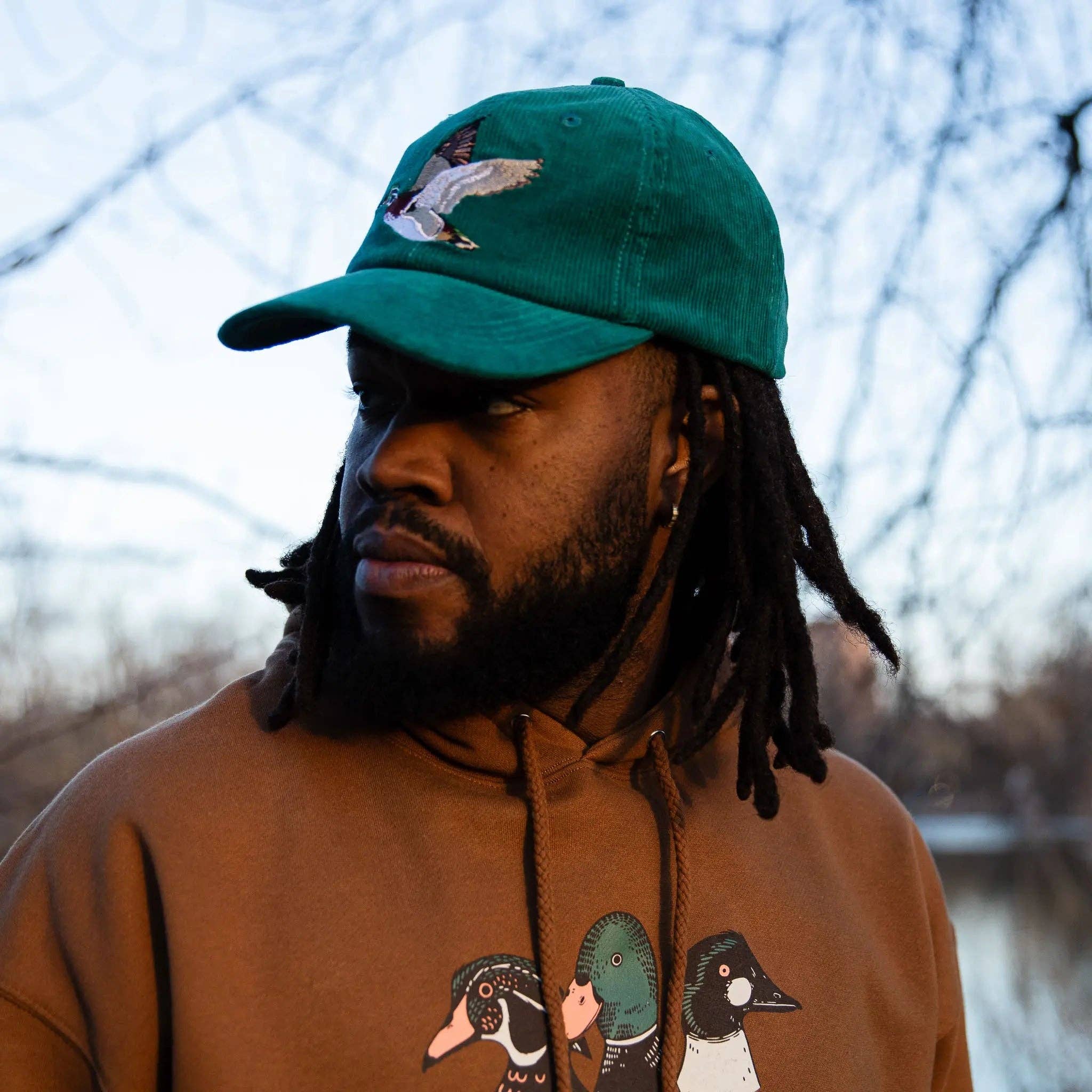 Person wearing a green cap and brown hoodie with duck designs outdoors