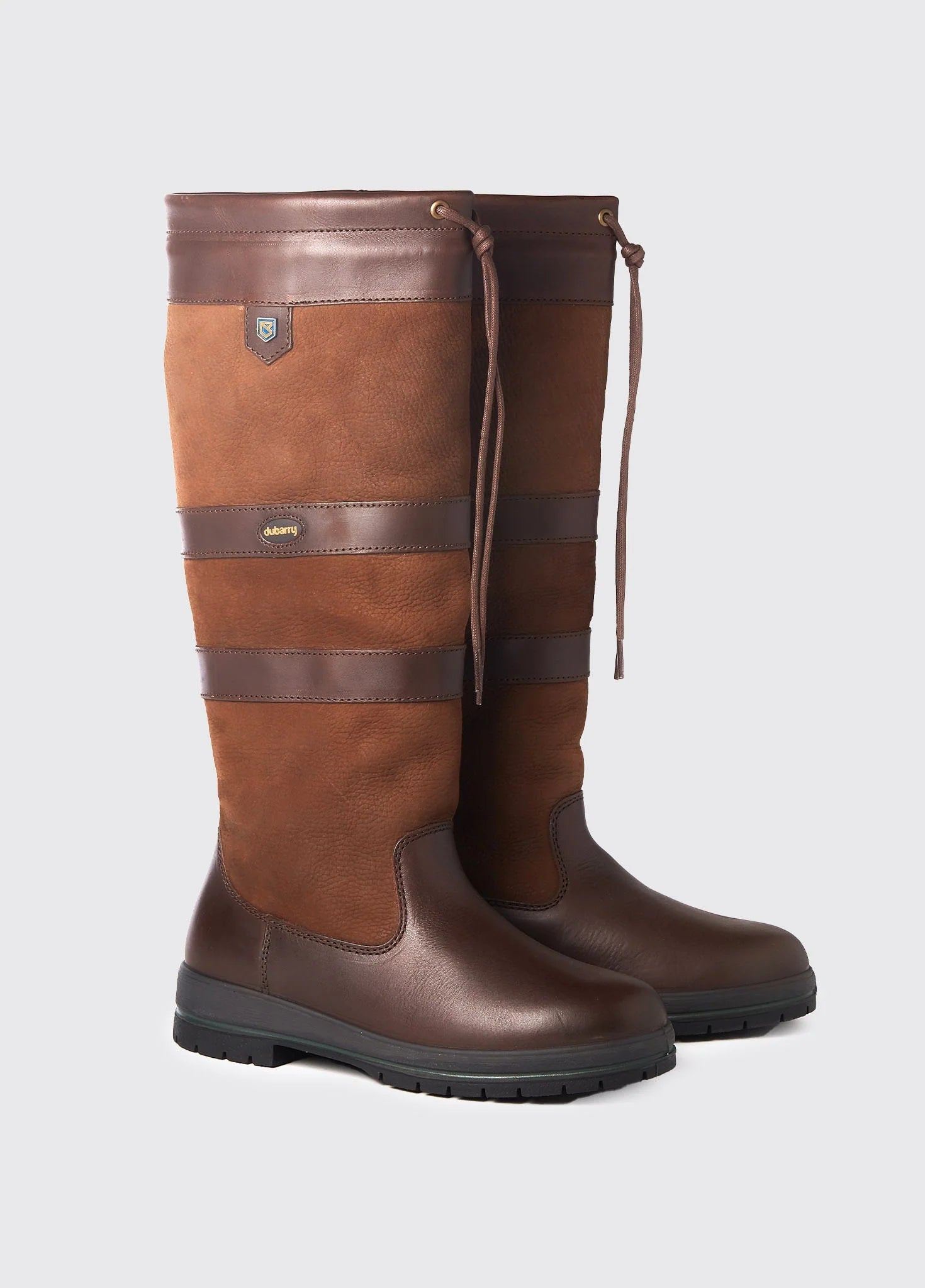 Pair of brown riding boots with leather straps on a light gray background
