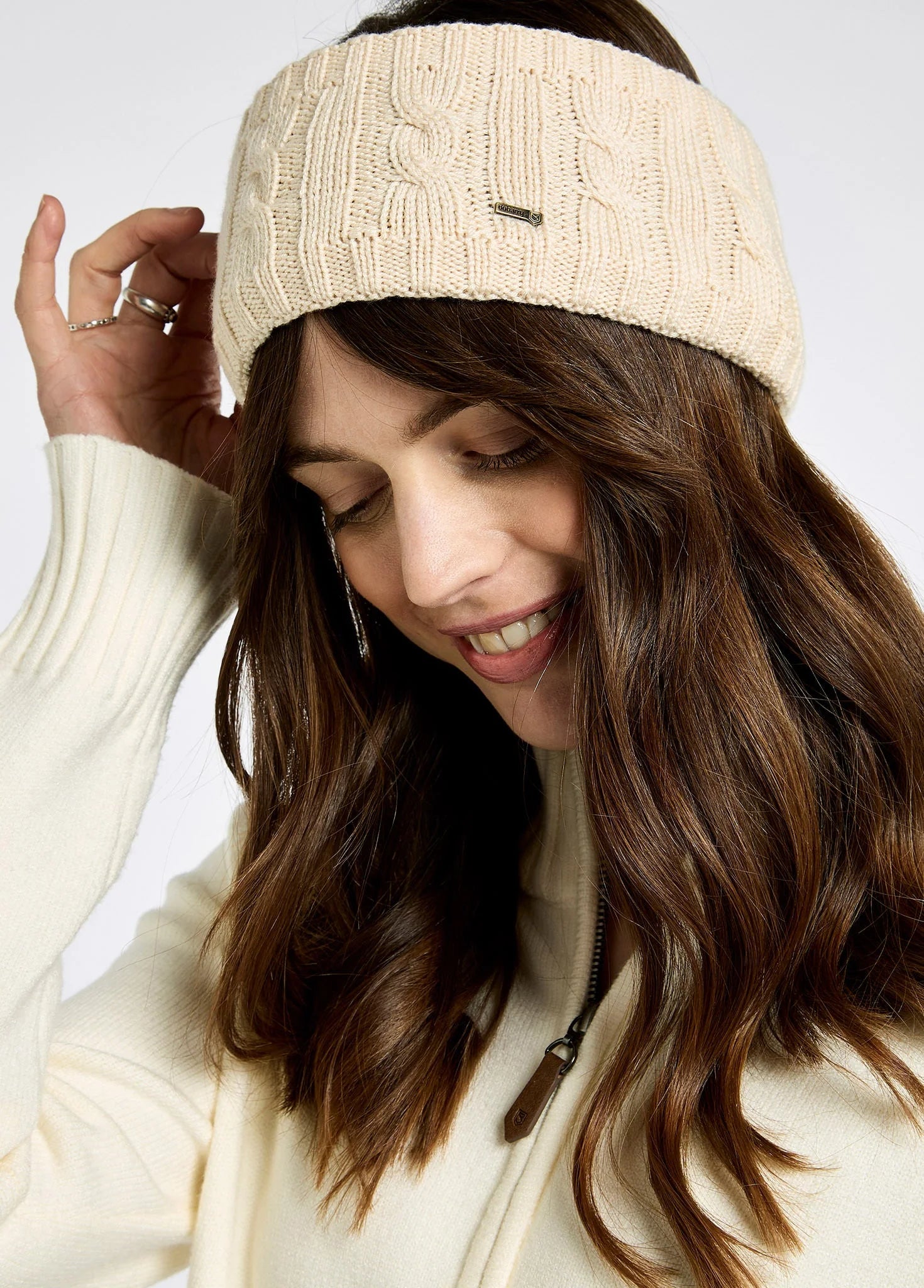 Woman wearing a beige knitted headband against a plain background