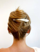 Back view of a person with styled hair and a hair clip on a plain background