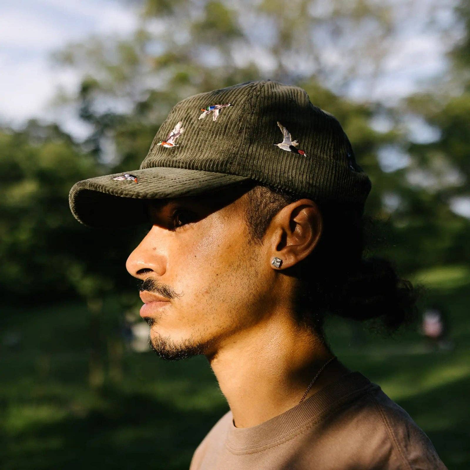 Man wearing a green cap with embroidered designs outdoors