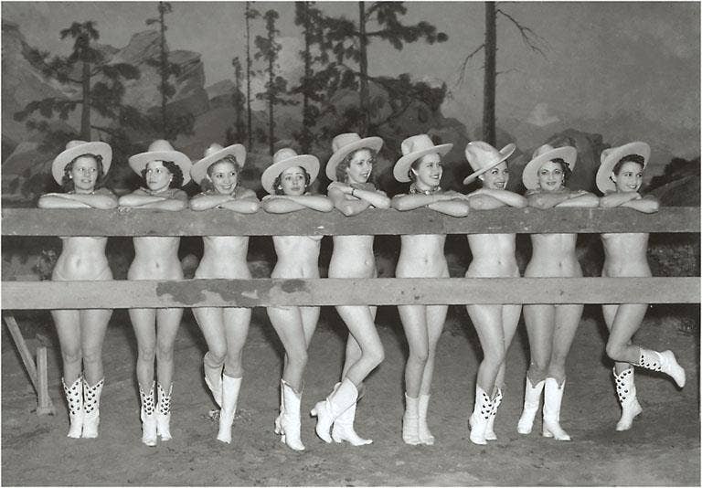 Vintage black and white photo of women in cowboy hats and boots posing outdoors.