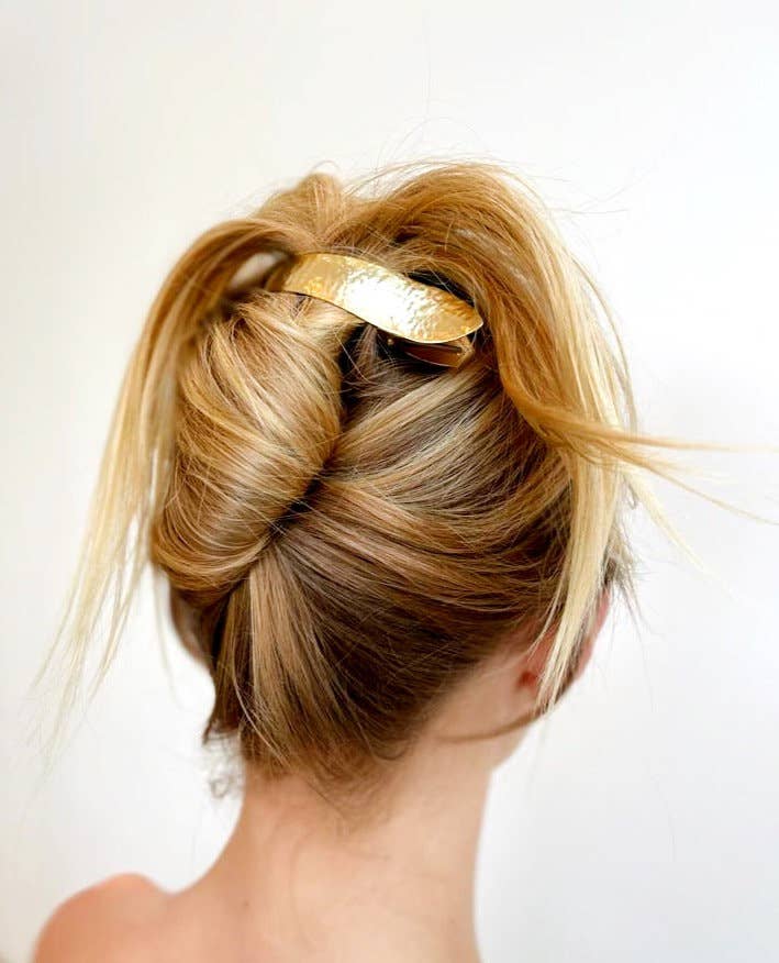Blonde hair styled in an updo with a gold hair accessory on a white background