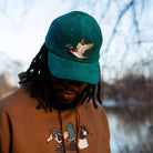 Person wearing a green cap with a duck design and a brown hoodie with duck designs outdoors.