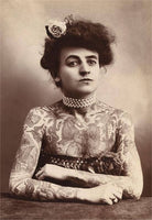 Vintage photograph of a woman with tattoos on her arms, wearing a pearl necklace and a decorative headpiece.