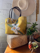 Yellow handbag with floral design on a wooden surface with a white textured wall background