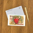 Vintage-style Valentine's Day postcard with a heart and angel illustration on a wooden surface with an envelope and pen.