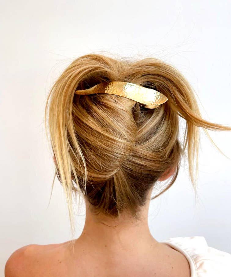 Blonde hair styled in an updo with a gold hair accessory on a white background