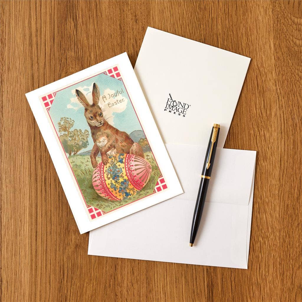Vintage-style Easter card with a rabbit on a wooden surface, featuring a pen and envelope.