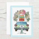 Illustration of a vintage car with floral decorations and suitcases on a light blue background.