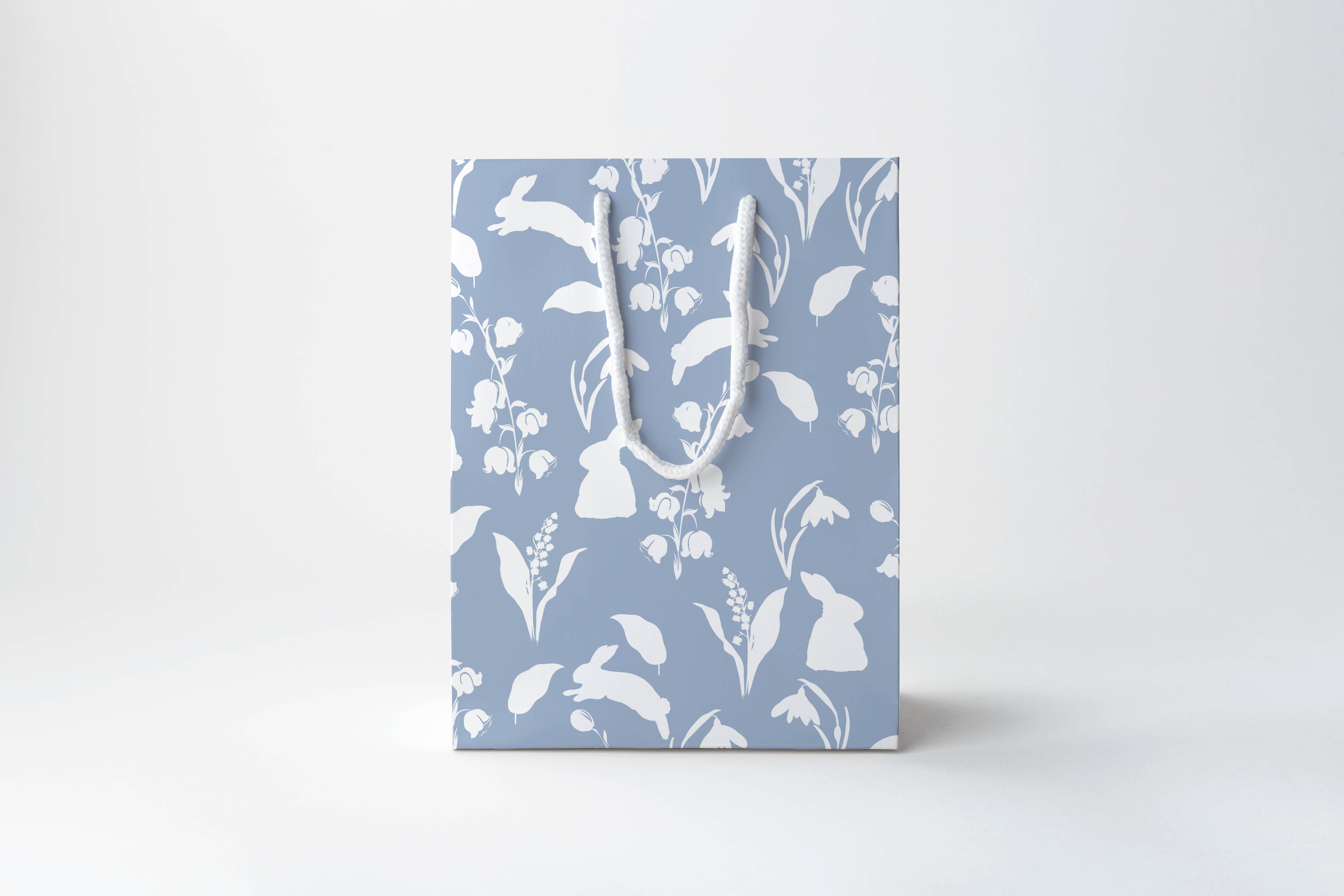 Gift bag with floral pattern and white handles on a light gray background