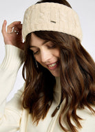 Woman wearing a beige knitted headband against a plain background